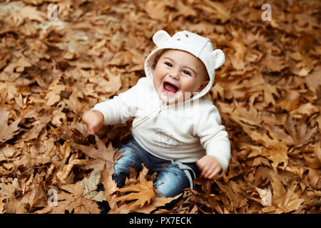 Adorable petit garçon assis dans le tas de feuilles d'arbres secs et rire, profiter de la beauté et de la chaleur de l'automne Banque D'Images