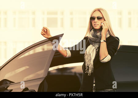 Fashion Business Woman talking on cell phone en dehors d'une voiture. Modèle féminin élégant et blazer noir portant des lunettes Banque D'Images