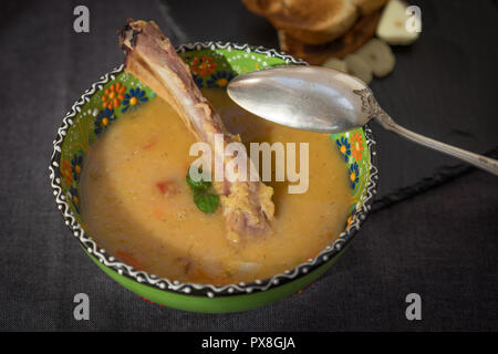 Soupe aux lentilles rouges avec côtes levées fumées dans un bol vert clair avec l'ornement floral. Fond tissu gris foncé. Banque D'Images