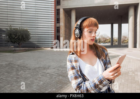 Une jeune femme aux cheveux rouges hipster, utilise une application dans son smart phone pour envoyer un message texte et écouter de la musique Banque D'Images