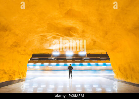 Vue panoramique de jeune homme debout dans une station de métro de banlieue à regarder passer les trains en heures de pointe, Stockholm, Suède Banque D'Images