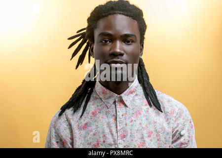 Beau jeune homme africain portant des fleurs shirt contre fond jaune Banque D'Images