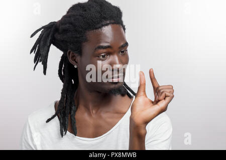 L'homme à la peau sombre montrant petite chose tout en souriant et debout près de fond blanc Banque D'Images