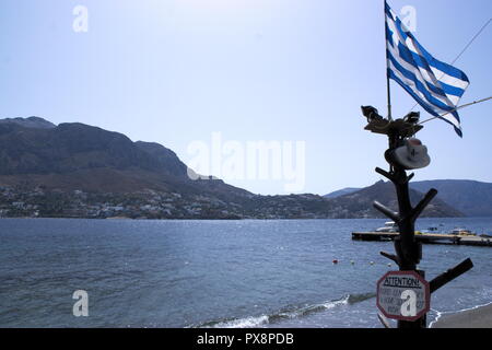 Grèce, l'île calme et paisible de Telendos. Vue sur l'île voisine de Kalymnos. Le drapeau grec flotte dans la brise estivale. Banque D'Images