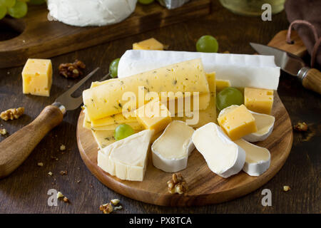 Assiette de fromage. Assortiment de fromages, les raisins et les noix sur la table rustique en bois sombre. Banque D'Images