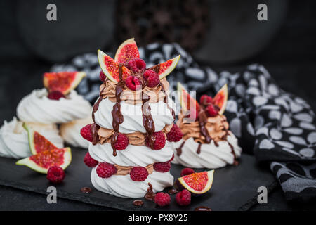 De délicieux gâteaux à la meringue Pavlova décoré de crème au chocolat, figues fraîches et framboises sur fond sombre Banque D'Images