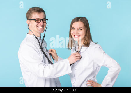 Deux meilleurs travailleurs professionnels smart smiling doctors en blouse blanche à l'écoute de l'autre signal avec stéthoscope sur fond bleu Banque D'Images