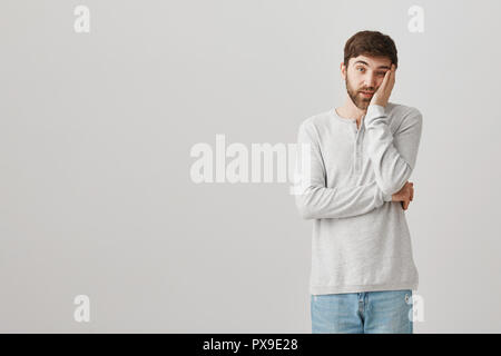 Tenir de temps dois-je écouter ce gars stupide. Portrait de l'ennui et stupéfié male student leaning head sur palm en étant debout sur fond gris, étant fatigué des discours politicien Banque D'Images