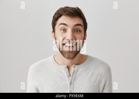 Guy excité audience dans toutes les oreilles pour dernière rumeurs qui se propagent dans le bureau. Emotive drôle jeune homme avec barbe tenait avec plus de l'expression surprise de mur gris, souriant et s'intéresser à la conversation Banque D'Images