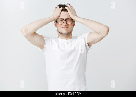 L'esprit gonna blow-up. Portrait de pressions et de jeunes hommes en colère en détresse nomade numérique tenant les mains sur les cheveux de fermer les yeux et intense sensation de tête plus souriant le stress, ne pas s'en sortir avec des dates Banque D'Images