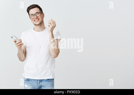 Guy décollant un écouteur pour entendre ce qu'ami souriant joyeusement goût nouveau single du chanteur préféré écouter la musique dans d'écouteurs avec application pour smartphone qui satisfait au fond gris Banque D'Images