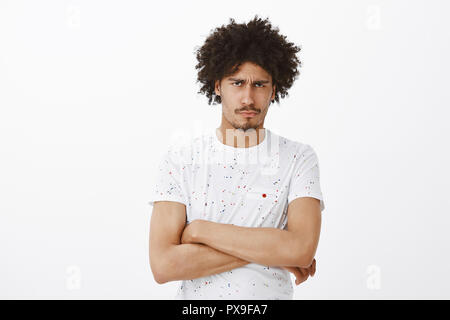 En attente d'excuses. Portrait de l'homme offensé mécontent sombre cute avec la peau foncée et les cheveux bouclés, tenant les mains croisées, la tête et les sourcils de colère, sentiments d'être insulté sur fond gris Banque D'Images