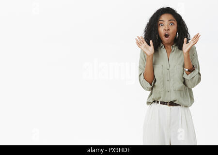 Woman getting choqués d'être effrayé de bruit soudain. Stupéfait attrayant élégant adult businesswoman en chemise et pantalon raising arms à partir de l'étonnement et la bouche d'ouverture de l'appareil photo à Banque D'Images