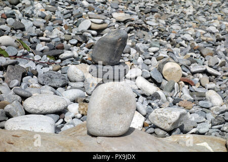 L'équilibre entre trois pierres au sommet d'un autre sur une plage de galets près de l'estuaire à Traeth Dulas sur l'île d'Anglesey Sentier du littoral, le Pays de Galles, Royaume-Uni. Banque D'Images