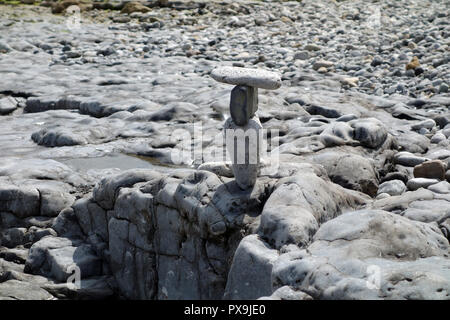 L'équilibre entre trois pierres au sommet d'un autre sur une plage de galets près de l'estuaire à Traeth Dulas sur l'île d'Anglesey Sentier du littoral, le Pays de Galles, Royaume-Uni. Banque D'Images