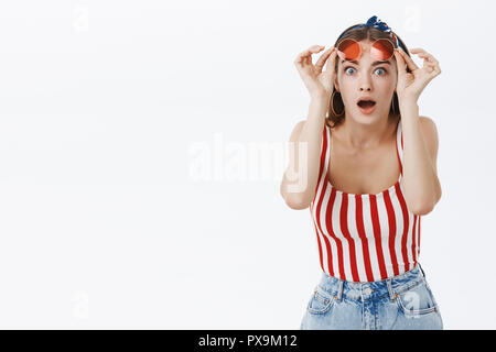 Taille plan sur étonné stupéfait attrayant mode femme en haut rayé l'abandon de la mâchoire en surprise d'être impressionné et étonné de lunettes avec une rumeur sur mur gris Banque D'Images