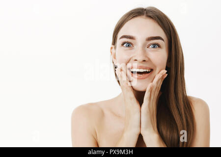 Close-up shot of impressionné et ravi les jeunes bonne-femme à large sourire visiteur spa holding palms sur le visage d'être heureux par l'excellent résultat après cosmetological produit appliqué sur la peau Banque D'Images