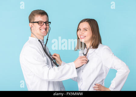 Deux meilleurs travailleurs professionnels smart smiling doctors en blouse blanche à l'écoute de l'autre signal avec stéthoscope sur fond bleu Banque D'Images