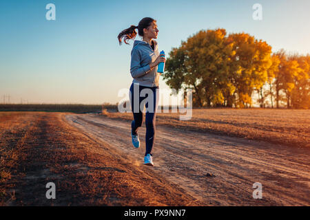 Woman holding bouteille d'eau dans le champ d'automne au coucher du soleil. Concept de vie sain. Sportifs actifs