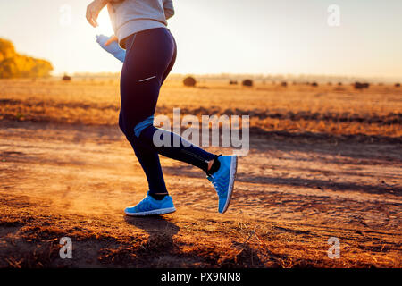 Femme d'exécution dans le champ d'automne au coucher du soleil. Concept de vie sain. Sportifs actifs. Close up de jambes