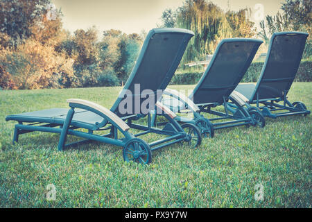 Repos et détente dans la nature. Rangée de trois roues vide chaises longues sur la pelouse verte et luxuriante en arrière-cour. Banque D'Images