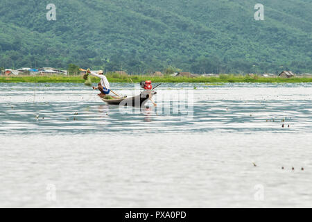 Jeune pêcheur avec net, accroupi sur un squat long boat, bateau traditionnel. L'équilibrage et des techniques de pêche. La région du lac Inle, Shan, Myanmar, Birmanie Banque D'Images