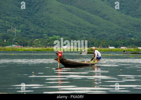 Jeune pêcheur avec net, accroupi sur un squat long boat, bateau traditionnel. L'équilibrage et des techniques de pêche. La région du lac Inle, Shan, Myanmar, Birmanie Banque D'Images