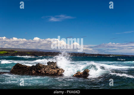 Vague se brisant sur la pierre de lave sombre ; spray blanc en l'air ; l'océan, le littoral et les nuages en arrière-plan. Plage de sable noir, punaluu, New York. Banque D'Images