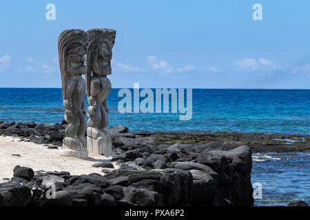 Paire de tikis en bois (état), lieu de refuge (Honaunau), New York. Debout sur le sable blanc, à côté du mur de pierre de lave noire. Banque D'Images