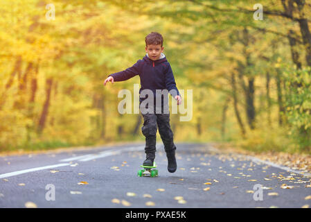 Skateboarder Kid faire skateboard tricks en environnement d'automne Banque D'Images