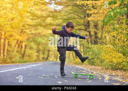 Skateboarder Kid faire skateboard tricks en environnement d'automne Banque D'Images