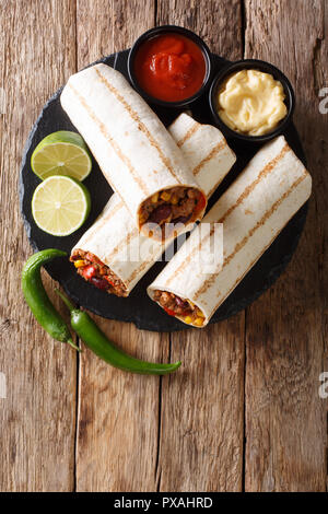 Grillé populaire mexicaine snack Burrito au boeuf et légumes et avec des sauces sur la table. Haut Vertical Vue de dessus Banque D'Images