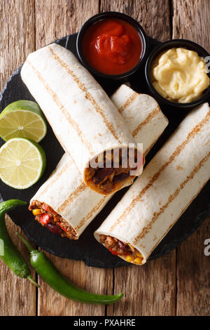 Burrito délicieux grillés farcis de viande hachée, les haricots, le maïs, le poivron et les tomates et avec des sauces sur la table. Vue du haut de la société abo verticale Banque D'Images