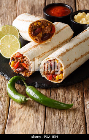 Burrito délicieux grillés farcis de viande hachée, les haricots, le maïs, le poivron et les tomates et avec des sauces sur la table. vertical, style rustique Banque D'Images