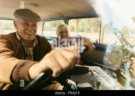 Smiling senior homme conduisant une vieille voiture avec une femme assise à côté de lui dans le siège passager. Happy senior couple partir en voyage. Banque D'Images