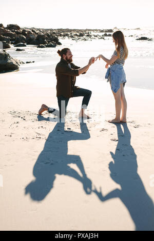Qui fait semblant de mettre un anneau au doigt, petite amie de la mer. L'homme vers le bas sur un genou mettre une bague de fiançailles sur le doigt de petite amie à plage. L'homme pr Banque D'Images