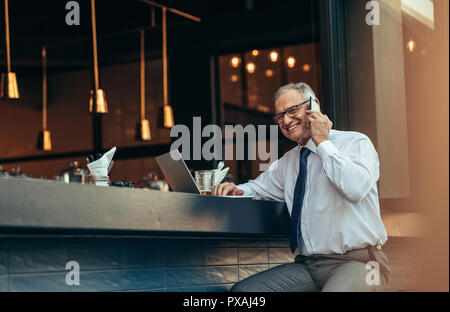 Smiling man sitting at usure formelle comptoir bar avec portable talking on cell phone. Senior entrepreneur faisant un appel téléphonique d'bar cou Banque D'Images