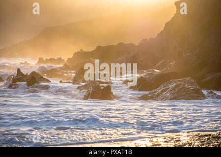 Coucher du soleil doré sur la côte du Pembrokeshire, dans le sud du Pays de Galles, UK.éclaboussures des vagues sur les rochers et brise du soir, falaises et brume en arrière-plan.paysage pittoresque. Banque D'Images