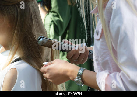 Une coiffure vents fille ses cheveux avec un fer à repasser. Close-up. Banque D'Images