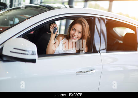 Happy woman conducteur en voiture blanche détient les clés de voiture dans sa nouvelle voiture chez car show room Banque D'Images