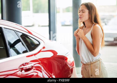 Visiter Agence de voiture. Belle jeune femme est l'étreindre nouvelle voiture. Banque D'Images