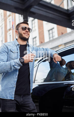 Cheerful conducteur en lunettes de soleil est en attente de son patron près de la Mercedes-Benz Banque D'Images