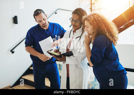 Groupe des médecins divers discuter d'un dossier patient dignosis debout ensemble dans un couloir de l'hôpital Banque D'Images