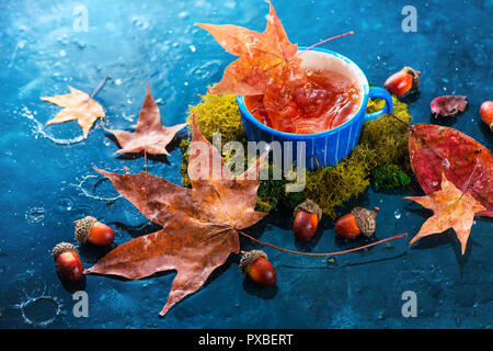 Touche de thé chaud dans une tasse en céramique bleue. Boisson d'automne photographie avec feuilles d'érable tombés sur un fond sombre avec copie espace. Banque D'Images