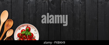 Divers cuillères en bois et les tomates dans une assiette avec du sel de l'Himalaya, le poivre et le basilic sur table en bois noir. Vue supérieure avec copie espace pour le menu ou d'une recette Banque D'Images