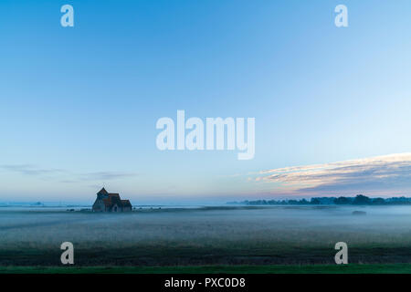Dawn blue sky over the lonely Thomas Becket une église à Fairfield sur Romney Marsh. Domaines couverts dans la brume, fixant le paysage. Pastel léger cloudson horizon. Certains moutons et vaches dans la brume. Vue à distance. Banque D'Images