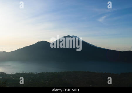 Lever du soleil sur de Gunung Batur volcano à Bali, Indonésie avec silhouette visible du Mont Agung pic volcanique recouverte de nuages et de brume Banque D'Images