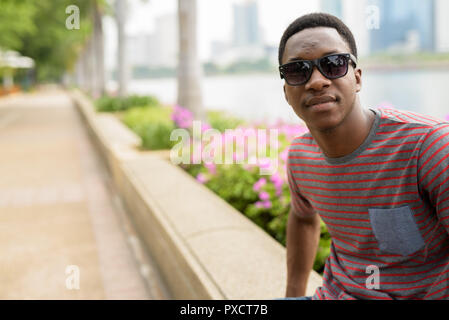 Beau jeune homme africain portant des lunettes de soleil et se détendre dans le parc Banque D'Images