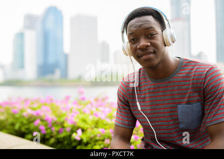 Beau jeune homme assis à l'Afrique park pendant l'écoute de la musique avec des écouteurs Banque D'Images