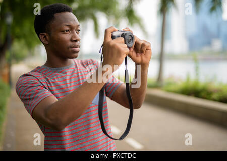 Beau jeune homme africain à prendre des photos avec camera in park Banque D'Images